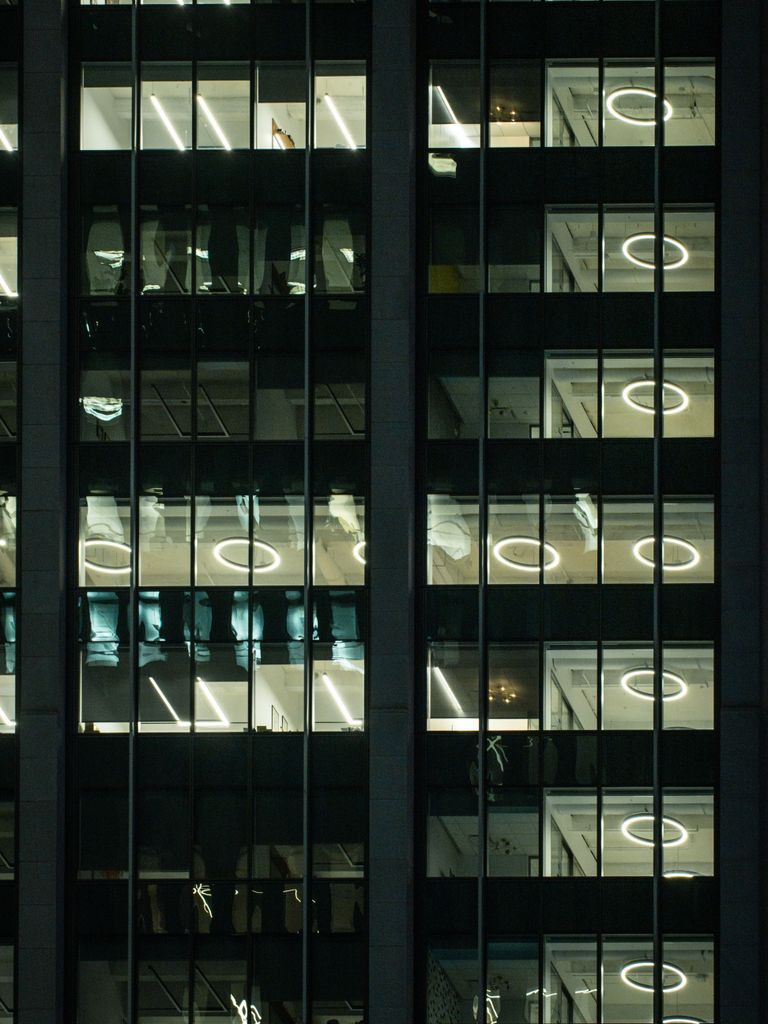 Vertical shot of a modern glass skyscraper at night, showcasing illuminated office windows.